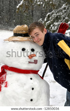 Frosty gets a hug from young man playing in the snow.  Snowman has straw hat, carrot nose, pipe, scarf and mittens.