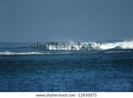 Active waves curl and roll toward shore.  Aqua and blue waters with blue sky.  Spray and foam.