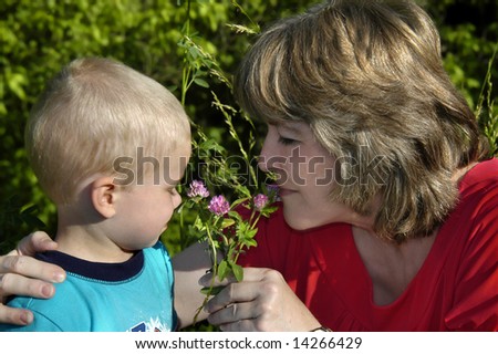 Grandmother and grandson share the wonders of nature as they smell some purple clover in a field.