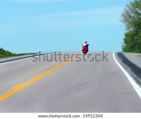 Cyclist rides into the wild blue yonder as his motorcycle tops a hill.  Red cycle.