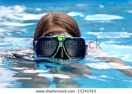 Big goggles emerge from swimming pool attached to young female teens head.