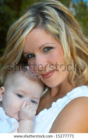Beautiful young mother holds her sleepy infant against her chest.  Baby is sucking her thumb.