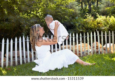 Mother and daughter play in garden.  White wooden picket fence in background.