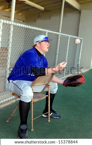 Baseball is tossed up and down as player waits for game to begin.  He is sitting in a metal chair backwards.