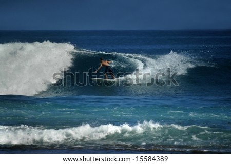Curling wave demands an agile athlete.  Male surfer swings back to enjoy more ride.