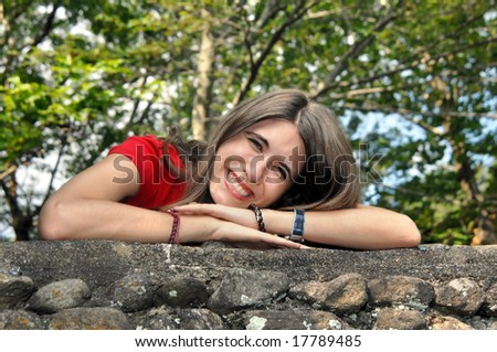 Female teen rests her head on her arms while posing on a rock wall.  Trees fill in background.