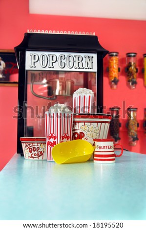 Counter has commercial sized popcorn popping machine, popcorn cartons, popcorn, dipper and butter.