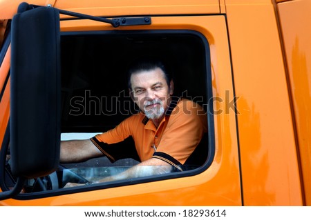 Truck driver sits in cab of his orange diesel truck.  His window is down and he is looking at camera.