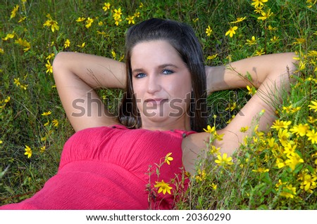 Attractive young woman lays in field of yellow wildflowers in a hot pink sleeveless top.