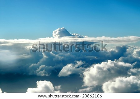 Small cloud head peaks through a layer of stratus.  Blue skies.