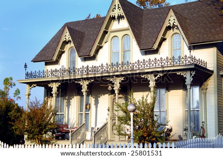 Authentic victorian home has balcony and three gables.  Morning light on tan wooden home.
