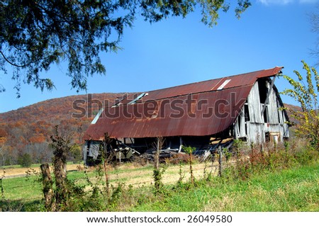 Blue skies and Ozark mountains frame rustic barn with tin roof.  Barbed wire fence and blue skies.
