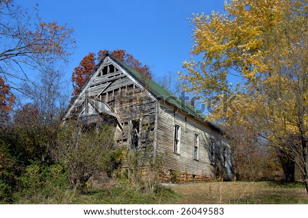Church stands abandoned and empty.  Golden leaves frame right side of photo.  Overgrown and deteriorating white wooden church with green roof.