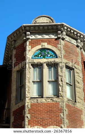 Flat Iron Flats building has stained glass window and is of stone and brick construction.  Blue skies frame building.