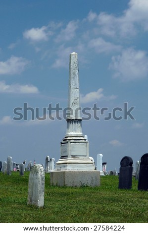 Tombstone is framed by blue skies.  Other markers form rows around tall ornate stone.