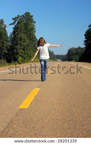 Struggling to balance, teen walks the yellow center line of highway.  Metaphor for \