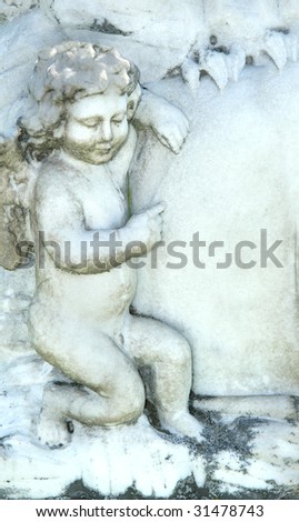 Angel points to the flat surface of a tombstone.  Old and weathered marble carved with a cherub and leaves.