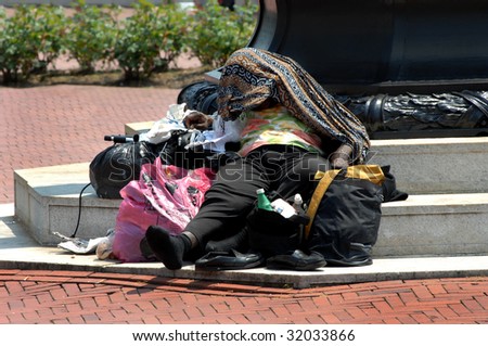 Homeless woman covers her head for relief from the suns heat while laying at the foot of a monument in downtown Washington DC.