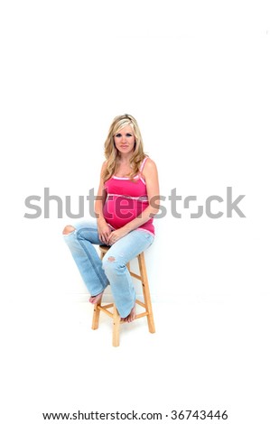 Expectant mom rests on a stool.  She is wearing grunge jeans and is barefoot.  Her jeans have holes at the knees and she is thinking wonderful thoughts about the coming baby.