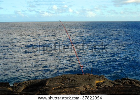 Fisherman has baited and set his rod to catch fish on the windward side of the Big Island of Hawaii.  Red rod sits on the cliff at MacKenzie State Park.