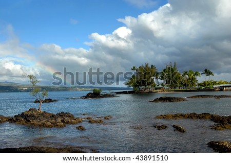 Small island on the Big Island of Hawaii is Coconut Island.  An arching metal bridge connects it to the mainland.  Recent rain storm leaves a rainbow over the Hilo area and bay.