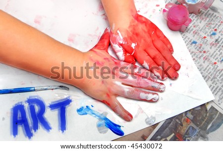 Little hands have created a masterpiece.  Paint smeared hands and paper.  Paintbrush in corner and the word art painted in blue.