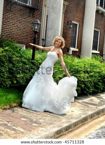 Beautiful young bride dances on the sidewalk before her wedding.  Large palatial home stands in background.  Bride is smiling happily.