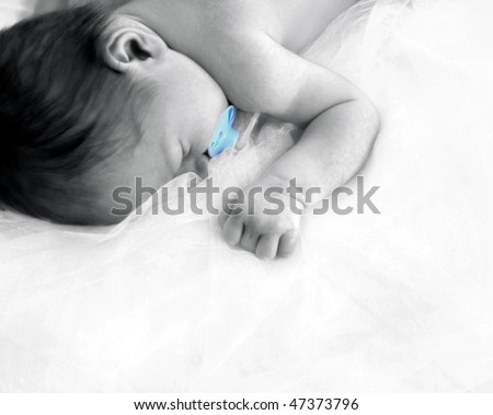 Tiny newborn sleeps in peace free of stress and worries.  He is laying on layers on netting in the corner of photo.