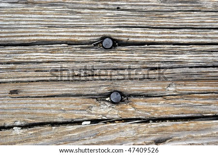 Old and aging boards are cracked with age.  Two large nail heads extrude from cracks in the wood.