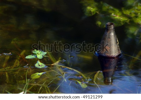 Beer bottle floats in a ditch.  Bottle is half submerged and littered the stagnant water in a North Louisiana ditch.