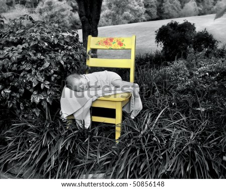 Tiny baby lays on a striped blanket on a yellow, wooden chair.  Chair sits surrounded by trees and lush foliage.