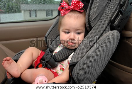 Infant sits in a car seat buckled up for safety.  She is making a funny face as this is not her favorite place to be.