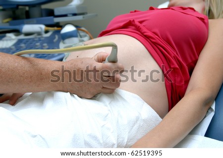 Technician performs an ultrasound of an expectant mother.  Closeup showing stomach and technician\'s hand.