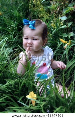 Little child sits in deep grass with a finger to her lips.  She is trying to decide if she should sit and enjoy nature some more or crawl on to another place to explore.