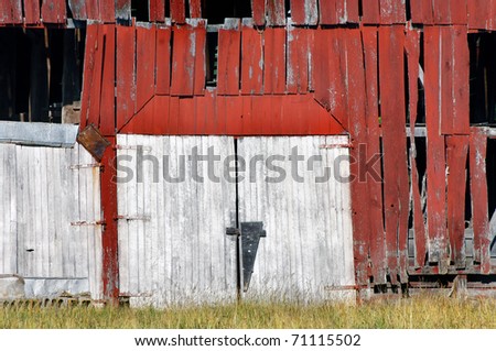 Double barn doors are boarded shut and historic building is abandoned.  Red, wooden, weathered and overgrown, this barn is derelict and dejected.