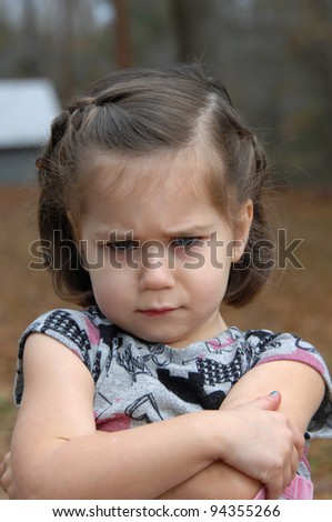 Arms crossed and eyebrows puckered, this little girl is upset and pouting.  She is standing outside and image is closeup.