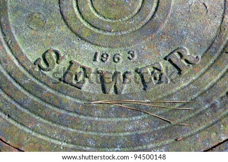 Sewer cover plate is heavy iron with ring design.  The letters spelling sewer are raised metal.  Rustic plate has the date 1963.