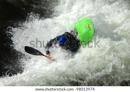 Kayaker goes under the boiling water on a raging river in North Carolina.  His kayak is green and his helmet is blue.