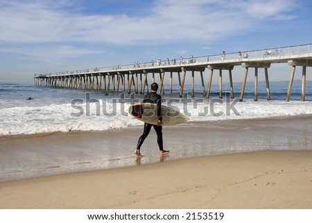 a young man is walking along the beach ready to go surfing