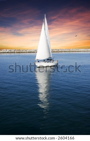 Sailboat with full sail is sailing on flat blue water with a sunset sky.