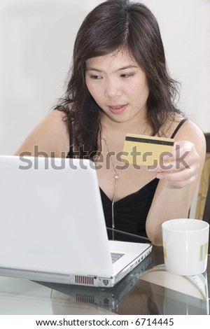 Pretty Asian woman with notebook computer and credit card sitting at table