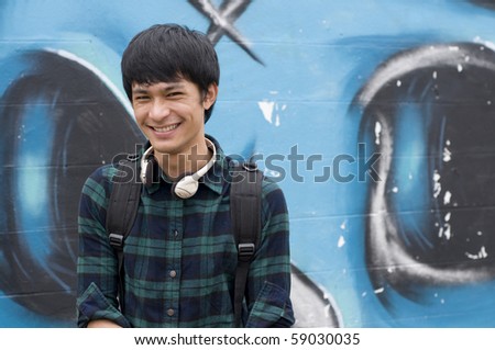 Asian teenage student wearing headphones in front of graffiti wall