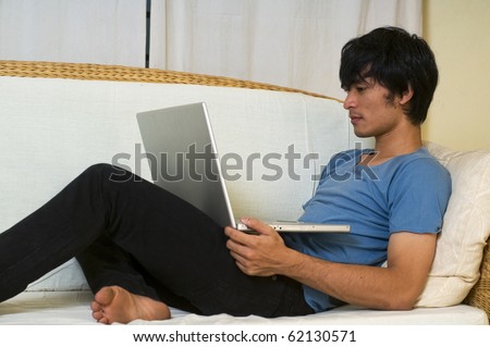 Young Asian man laying on sofa using computer for social networking