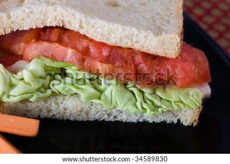 Tomato and butter lettuce sandwich on a black plate with carrot sticks on the side.