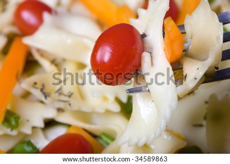 Fork with a bite of pasta, tomato, and orange bell pepper above a plate of the food.