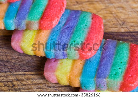 Rainbow cookies are stacked on each other on a wood cutting board.