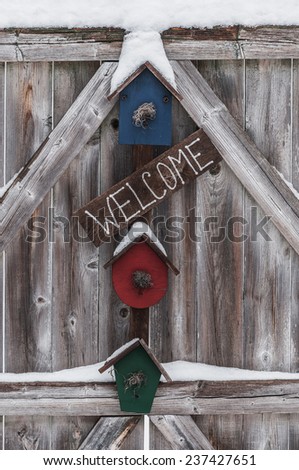 Residential welcome sign, trimmed with  some light snow, hanging on a rough exterior fence gate..