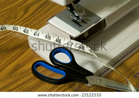 Detail view of sewing machine foot, scissors, and a tape measure.
