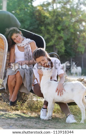 two young happy women with cat and goat on farm outdoor portrait