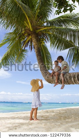 three children - boy and girls - sitting on palm tree on tropical beach background